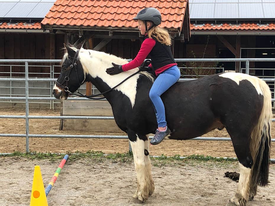 Kind reitet auf unserem schwarz-weißen Pony Jam auf dem Reitplatz